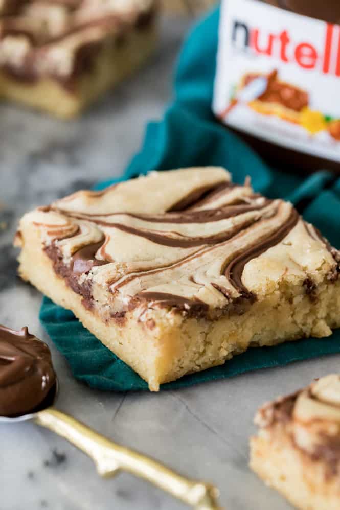 Soft and chewy Nutella blondies are made with a buttery cookie base and topped off with ribbons of rich Nutella swirls! These cookie bars are so easy to make, and everyone who tries them is going to want the recipe! A Nutella Blondie square.