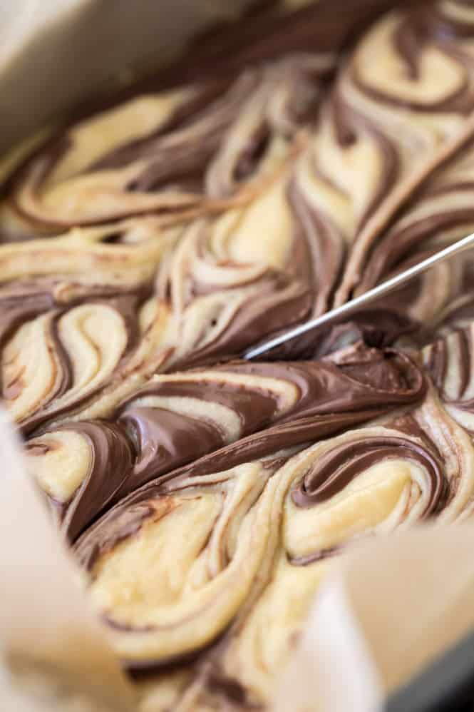 Soft and chewy Nutella blondies are made with a buttery cookie base and topped off with ribbons of rich Nutella swirls! These cookie bars are so easy to make, and everyone who tries them is going to want the recipe! Nutella blondies being sliced in a pan.