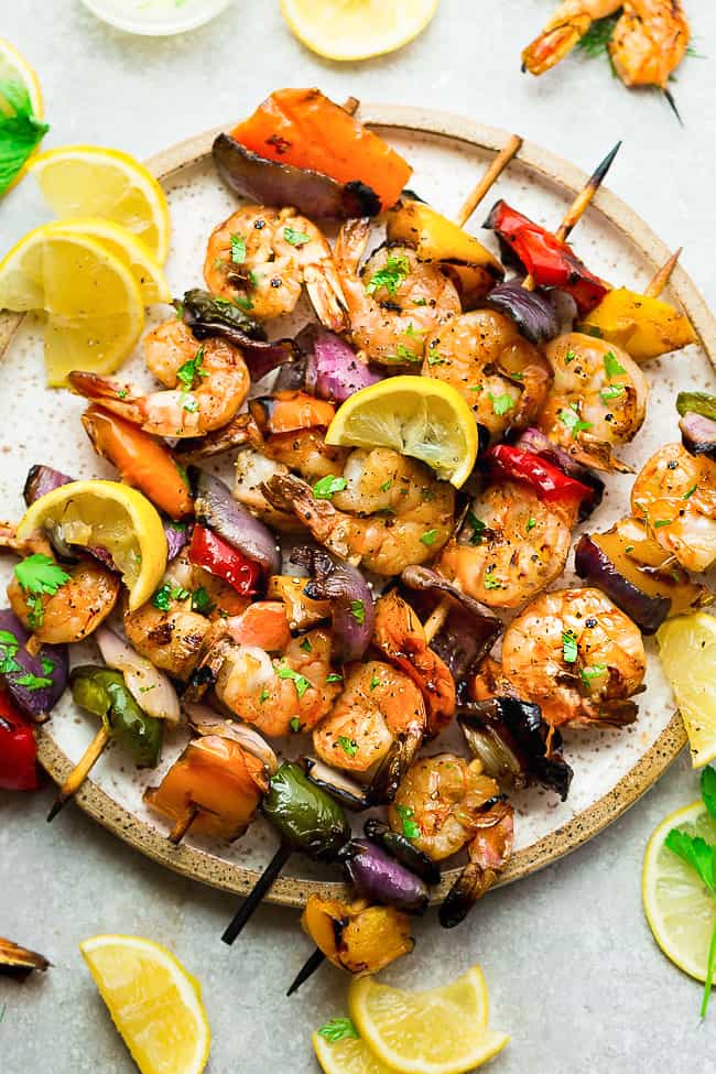 Grilled Lemon Garlic Butter Shrimp with Vegetables - a simple and tasty recipe for summer grilling. Juicy shrimp and tender veggies are coated in an amazing buttery lemon garlic blend that are grilled to perfection. Grilled Lemon Garlic Butter Shrimp with Vegetables on a white plate.