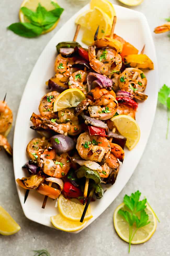 Grilled Lemon Garlic Butter Shrimp with Vegetables - a simple and tasty recipe for summer grilling. Juicy shrimp and tender veggies are coated in an amazing buttery lemon garlic blend that are grilled to perfection. Grilled Lemon Garlic Butter Shrimp with Vegetables on a white platter.