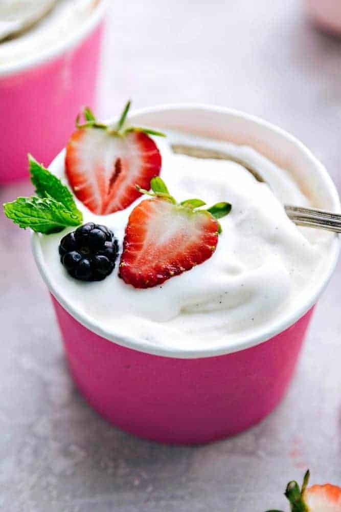 This vanilla soft serve frozen yogurt is delicious and perfect for the hot summer days! Everyone goes crazy for it! Vanilla soft serve frozen yogurt in a pink paper cut with two strawberries and a blackberry on top with a metal spoon.