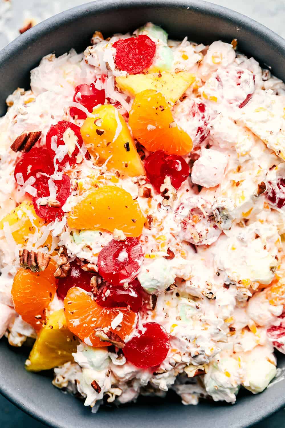 Ambrosia Salad is filled with mandarin oranges, pineapple, maraschino cherries, coconut, and marshmallows and mixed in a fluffy cool whip! This is a potluck classic! Close up on ambrosia salad.