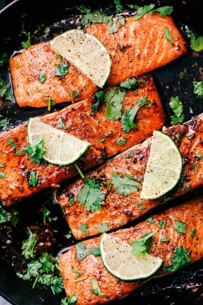 Cilantro Lime Butter Salmon is pan seared to tender and flaky perfection and has the most amazing cilantro lime butter honey sauce on top! Cilantro Lime Butter Salmon in a skillet with sliced lime on top.