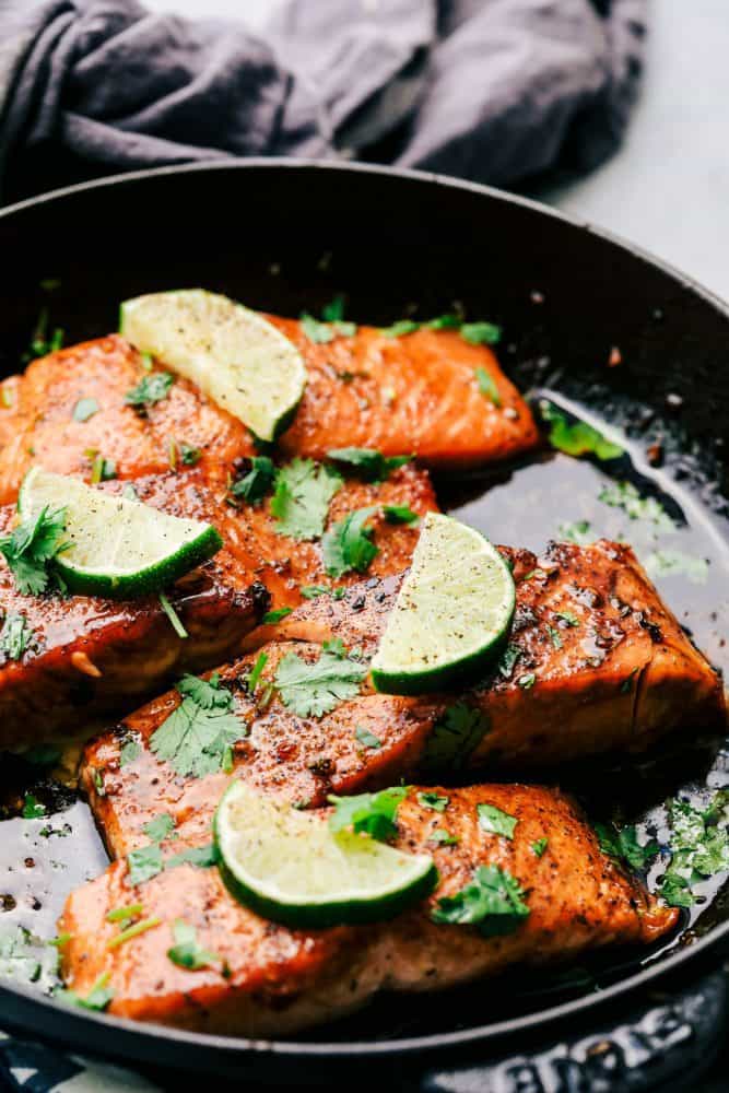 Cilantro Lime Butter Salmon is pan seared to tender and flaky perfection and has the most amazing cilantro lime butter honey sauce on top! Cilantro Lime Butter Salmon in a skillet with sliced limes on top of the salmon.