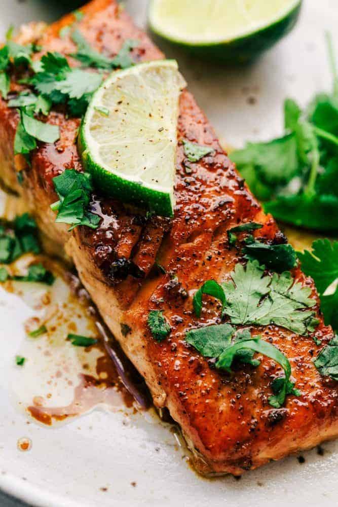 Cilantro Lime Butter Salmon is pan seared to tender and flaky perfection and has the most amazing cilantro lime butter honey sauce on top! Cilantro Lime Butter Salmon on a white plate with sliced lime on top.