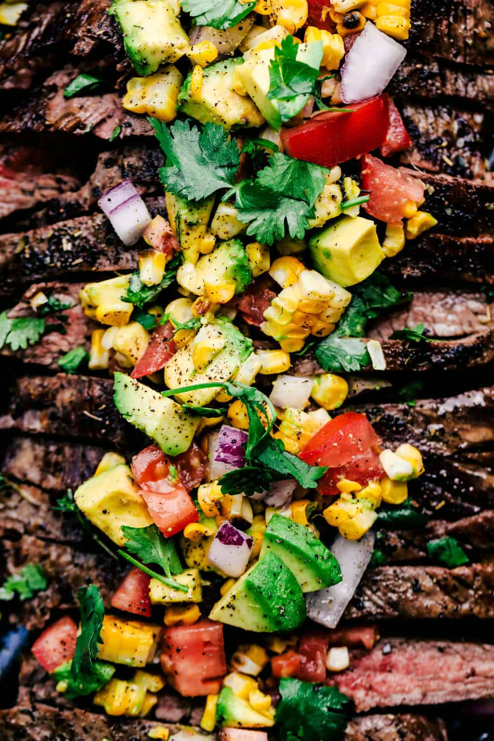 Grilled Garlic Herb Flank Steak with Avocado Corn Salsa is infused with amazing garlic herb flavor and grilled to tender and juicy perfection. The avocado corn salsa on top is phenomenal! Close up on grilled herb flank steak