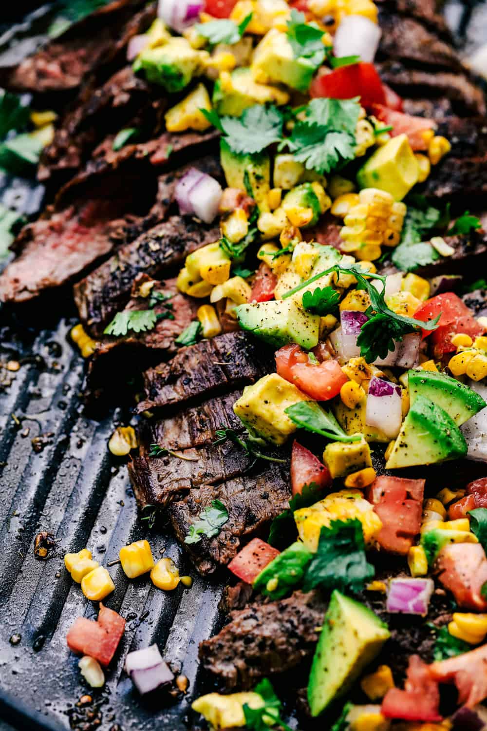 Grilled Garlic Herb Flank Steak with Avocado Corn Salsa is infused with amazing garlic herb flavor and grilled to tender and juicy perfection. The avocado corn salsa on top is phenomenal! Grilled flank steak on a skillet.