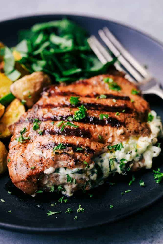 Grilled Spinach and Herb Stuffed Pork Chops are so easy to make and stuffed with a creamy parmesan spinach and herb mixture that takes these delicious and full of flavor pork chops to the next level! Grilled Spinach and Herb Stuffed Pork Chops on a black plate with a metal fork.