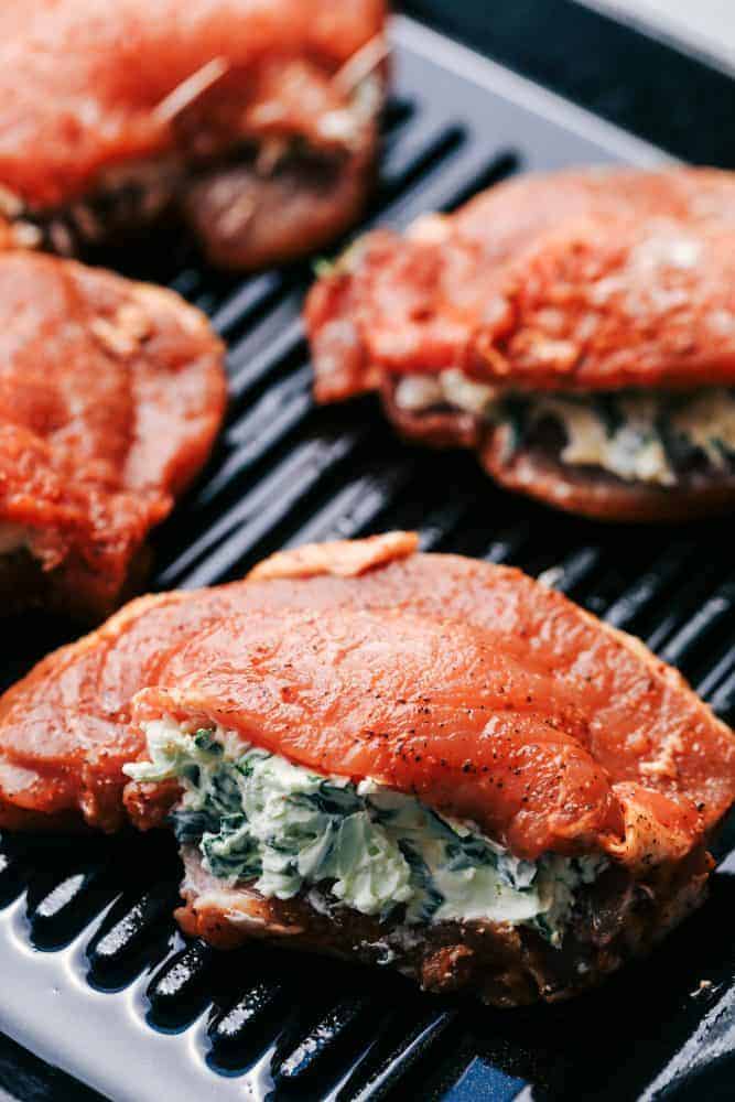 Grilled Spinach and Herb Stuffed Pork Chops are so easy to make and stuffed with a creamy parmesan spinach and herb mixture that takes these delicious and full of flavor pork chops to the next level! Uncooked herb stuffed pork chops on a grill pan.