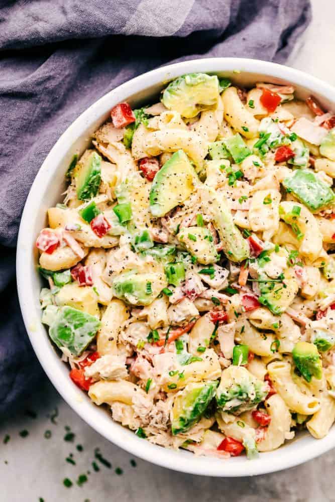 Tuna Avocado Macaroni Salad is an AMAZING creamy macaroni salad that is filled with chopped veggies, avocado, and tuna. This is going to impress everyone at your next potluck! Tuna Avocado Macaroni Salad in a white bowl with a grey cloth on the side.
