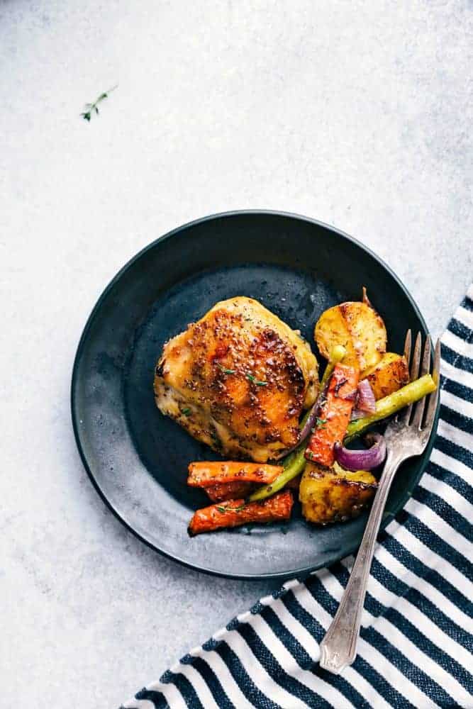 Delicious savory honey mustard chicken and root vegetables all cooked together on ONE sheet pan! Honey mustard chicken and root vegetables on a black plate with a white fork.