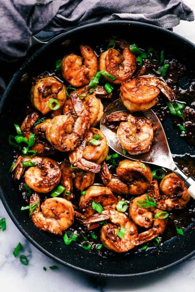 Cajun Garlic Butter Shrimp is made in the most amazing cajun garlic butter sauce. This is ready in 15 minutes and a meal that will wow the family! Cajun Garlic Butter Shrimp in a skillet with a metal spoon for serving.