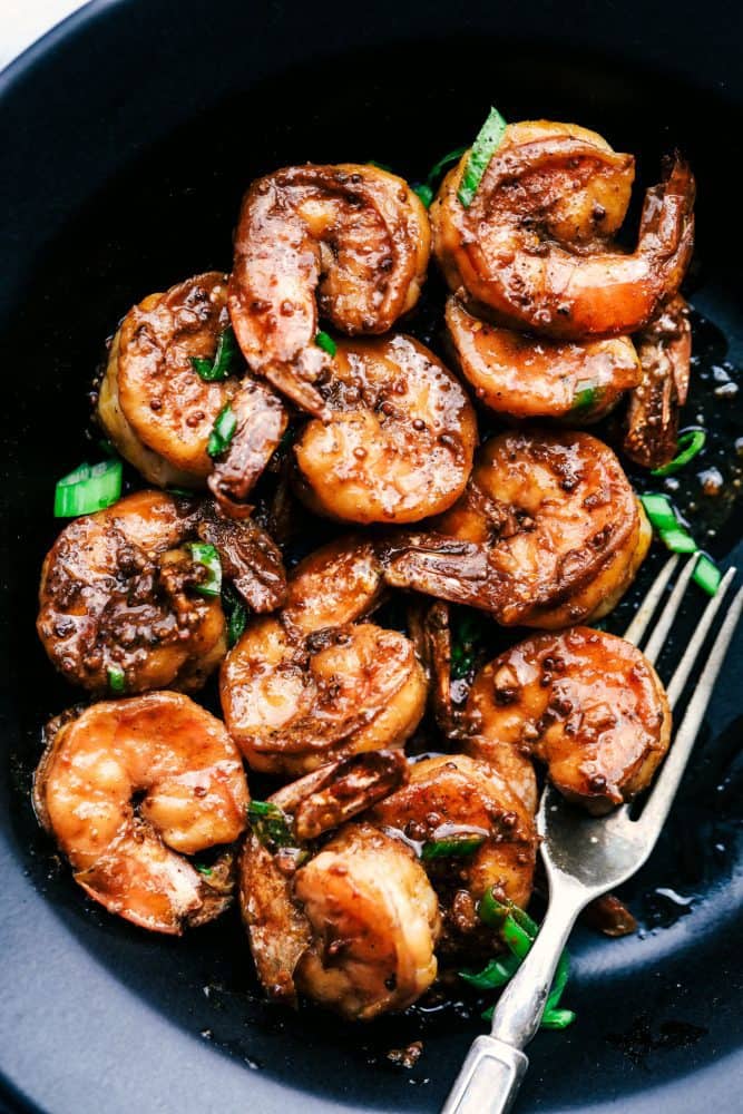 Cajun Garlic Butter Shrimp is made in the most amazing cajun garlic butter sauce. This is ready in 15 minutes and a meal that will wow the family! Cajun Garlic Butter Shrimp in a black bowl with a metal fork.