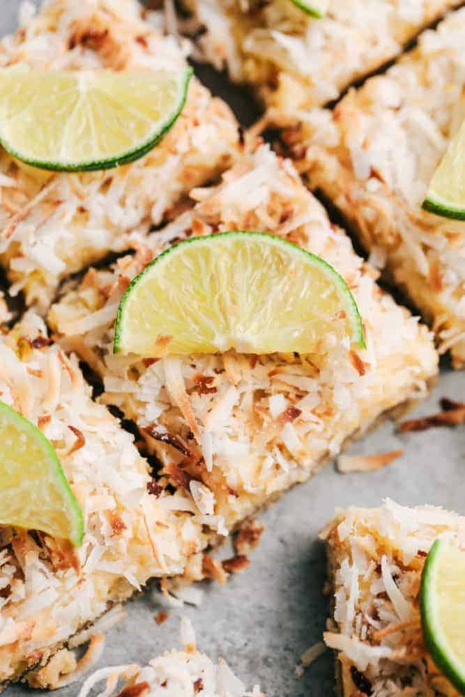 Coconut Lime Butter Bars have an amazing buttery brown sugar crust with a lime filling and topped with coconut flakes. These are the perfect cool and creamy summer bars!ย Close up of sliced Coconut Lime Butter Bars with freshly sliced lime on top.