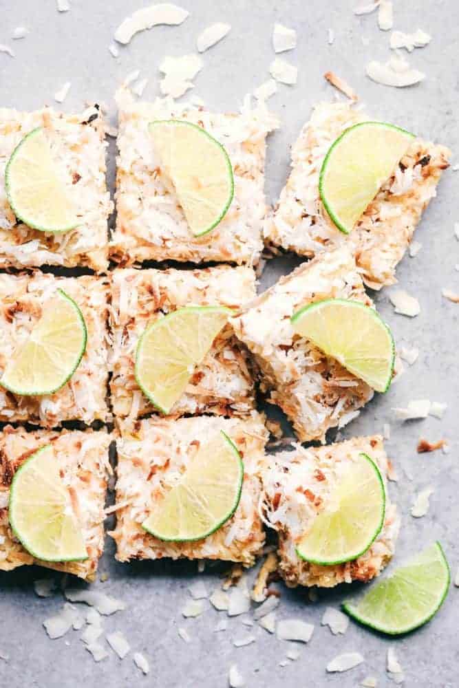 Coconut Lime Butter Bars have an amazing buttery brown sugar crust with a lime filling and topped with coconut flakes. These are the perfect cool and creamy summer bars!ย Cut Coconut Lime Butter Bars with fresh sliced limes on top.
