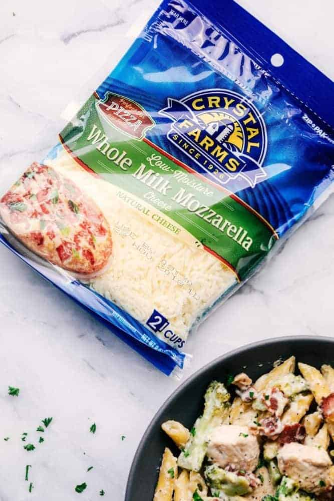 Cheesy Chicken, Bacon and Broccoli Ranch Pasta is a meal in one that is made in one pan and has such amazing creamy ranch flavor! This meal will be a hit with the entire family! Cheesy Chicken, Bacon and Broccoli Ranch Pasta in a grey bowl with a package of Crystal Farms Whole Milk Mozzarella Cheese.