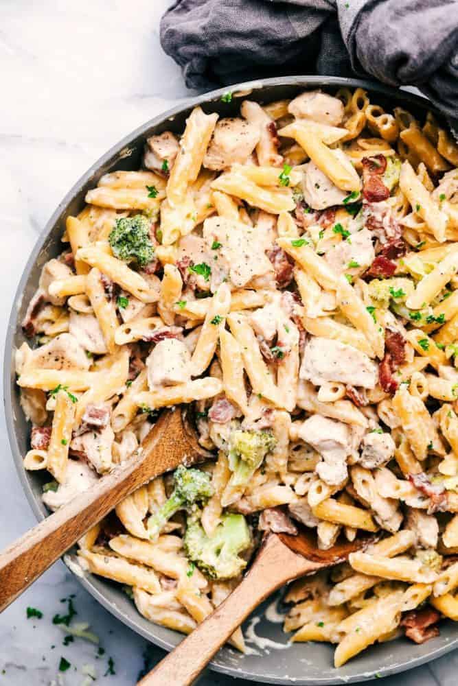 Cheesy Chicken, Bacon and Broccoli Ranch Pasta is a meal in one that is made in one pan and has such amazing creamy ranch flavor! This meal will be a hit with the entire family! Large bowl of Cheesy Chicken, Bacon and Broccoli Ranch Pasta with two wooden spoons for serving.