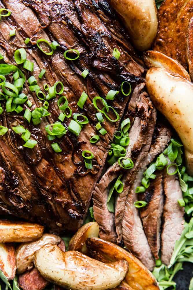 Brown Sugar Garlic Flank Steak is made with the most amazing brown sugar garlic soy marinade. The steak is grilled to perfection and melt in your mouth delicious!ย Close up of Brown Sugar Garlic Flank Steak with baked potato slices.