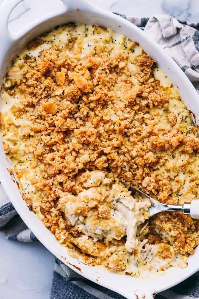 Poppyseed Chicken Casserole is such a classic dish that is incredibly easy to make! A creamy chickenย casserole topped with a buttery ritz topping. This will be the best you ever make!ย Poppyseed Chicken Casserole in a white platter with a metal spoon.