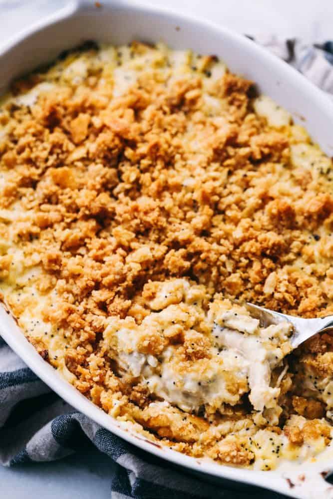 Poppyseed Chicken Casserole is such a classic dish that is incredibly easy to make! A creamy chickenย casserole topped with a buttery ritz topping. This will be the best you ever make!ย Poppyseed Chicken Casserole in a white platter with a metal spoon.