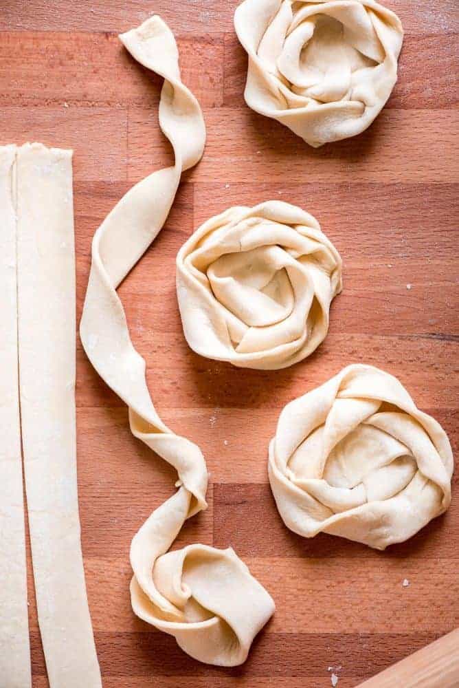 Apple Danishes are the perfect way to ring in the apple season! The flaky crust, apple pie filling, crumb topping, and simple glaze make them irresistible. Dough being rolled into danishes on a wood table.