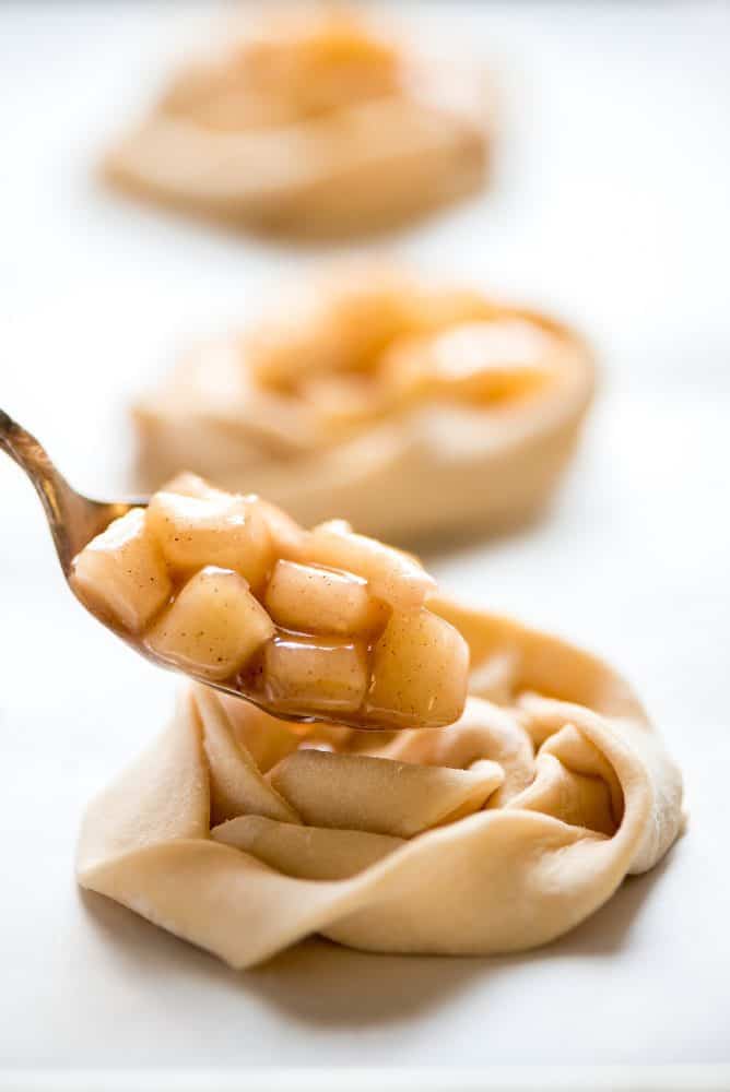 Apple Danishes are the perfect way to ring in the apple season! The flaky crust, apple pie filling, crumb topping, and simple glaze make them irresistible. Close up of un-cooked apple filling being placed on the dough.