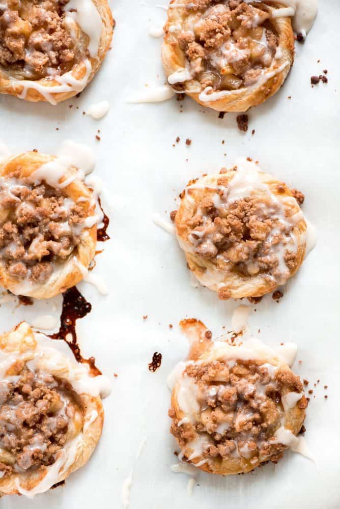 Apple Danishes are the perfect way to ring in the apple season! The flaky crust, apple pie filling, crumb topping, and simple glaze make them irresistible. Six Apple Danishes on a cooking sheet.