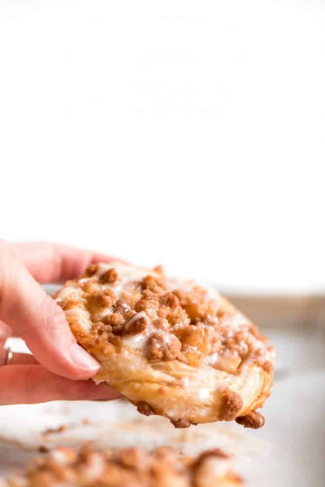 Apple Danishes are the perfect way to ring in the apple season! The flaky crust, apple pie filling, crumb topping, and simple glaze make them irresistible. Apple Danish fresh out of the oven being held.