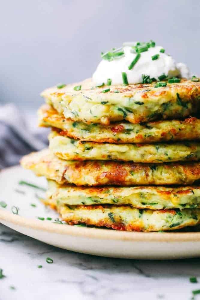 Cheesy Zucchini Fritters stacked on a white plate. 