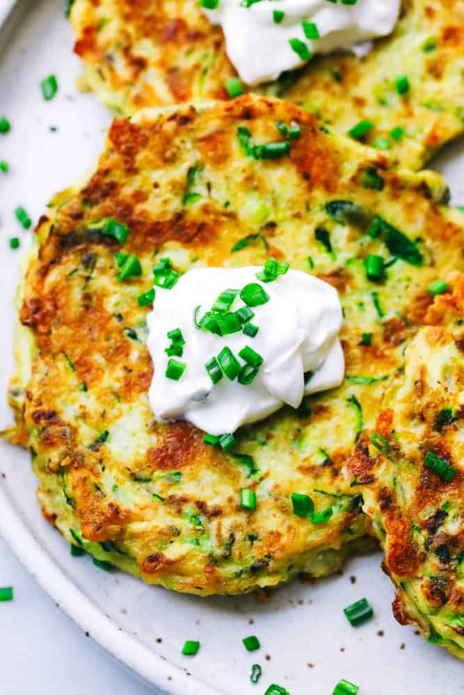 Cheesy Zucchini Fritters are filled with three cheeses and zucchini. These are savory and easy to make and the perfect way to use up that garden zucchini! Close up of Cheesy Zucchini Fritters on a white plate.