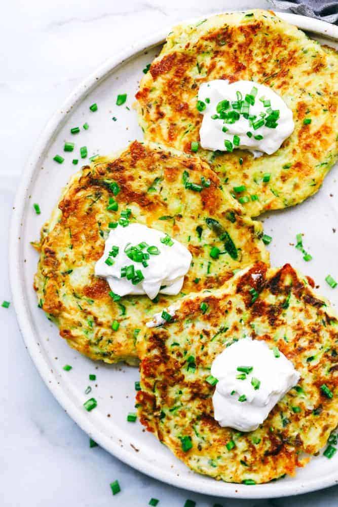 Cheesy Zucchini Fritters are filled with three cheeses and zucchini. These are savory and easy to make and the perfect way to use up that garden zucchini! Three Cheesy Zucchini Fritters on a white plate.