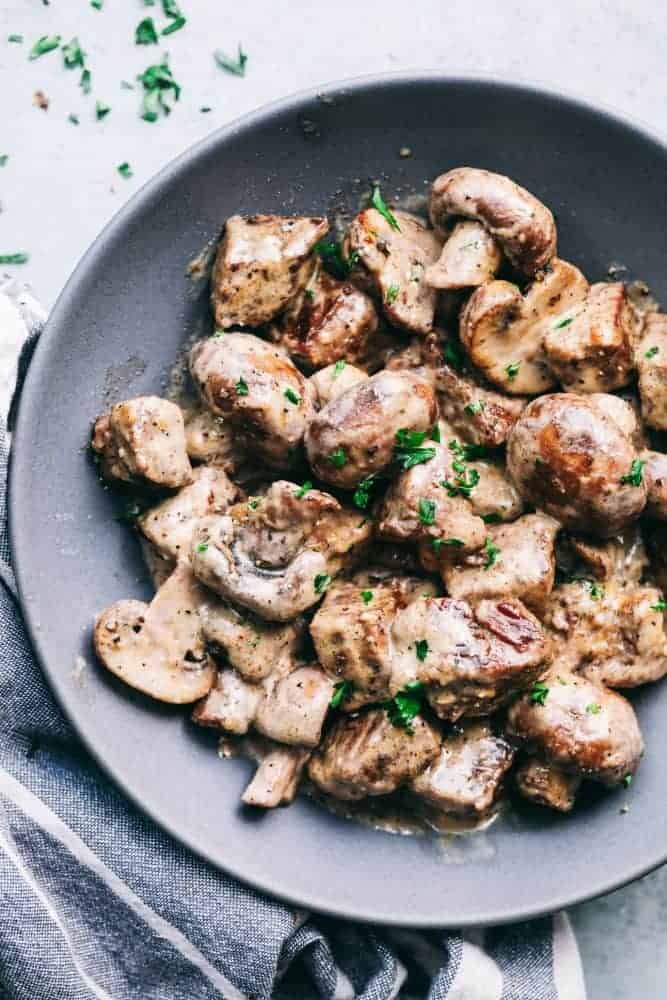 Creamy Garlic Steak Bites with Mushrooms are made in the most amazing creamy garlic sauce with melt in your mouth steak bites and mushrooms! Creamy garlic steak bites with mushroom served on a gray plate garnished with fresh parsley.