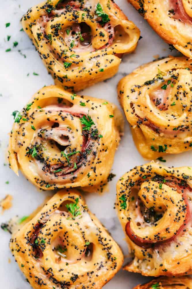 Hot Ham and Swiss Pinwheels have smoked ham and melty swiss cheese that are rolled up in croissantย dough and are brushed with a buttery garlic poppyseed topping! The perfect insanely delicious quick and easy dinner or appetizer! Close up of Hot Ham and Swiss Pinwheels after they have been cooked.