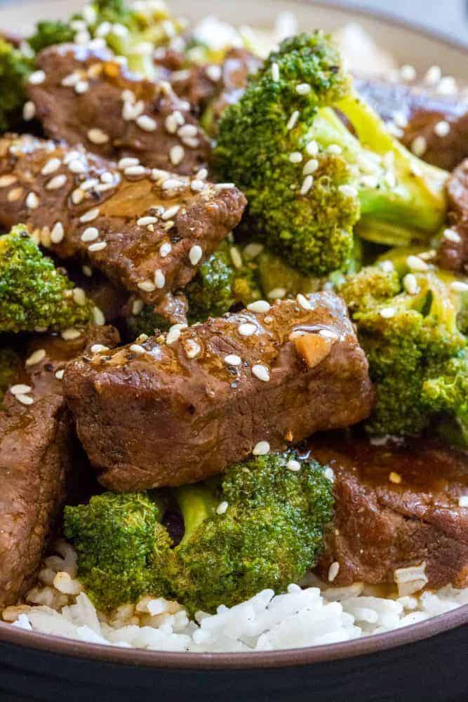 Instant Pot Beef and Broccoli is a flavorful Chinese meal made in minutes by pressure cooking. For this recipe slices of beef chuck are marinated in a sesame, soy, ginger, and garlic mixture. The beef is cooked until tender in a soy and oyster sauce base. Broccoli florets are steamed in the Instant Pot until crisp-tender. The dish can be served with rice and garnished with sesame seeds. Close up photo of beef and broccoli topped with sesame seeds.