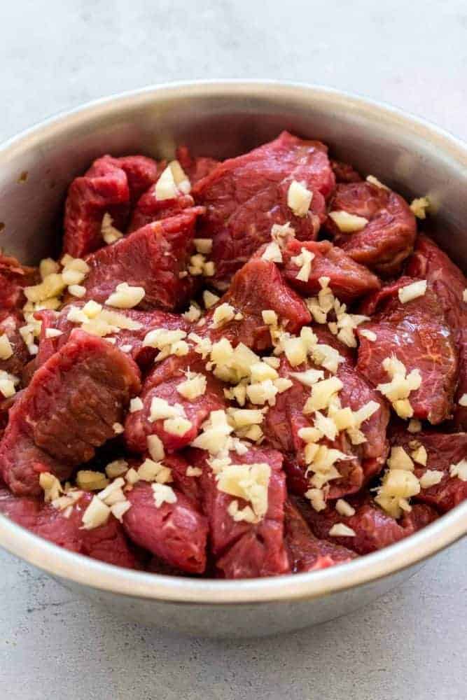 Instant Pot Beef and Broccoli is a flavorful Chinese meal made in minutes by pressure cooking. For this recipe slices of beef chuck are marinated in a sesame, soy, ginger, and garlic mixture. The beef is cooked until tender in a soy and oyster sauce base. Broccoli florets are steamed in the Instant Pot until crisp-tender. The dish can be served with rice and garnished with sesame seeds. Beef chuck in a bowl with raw pieces of garlic and ginger.