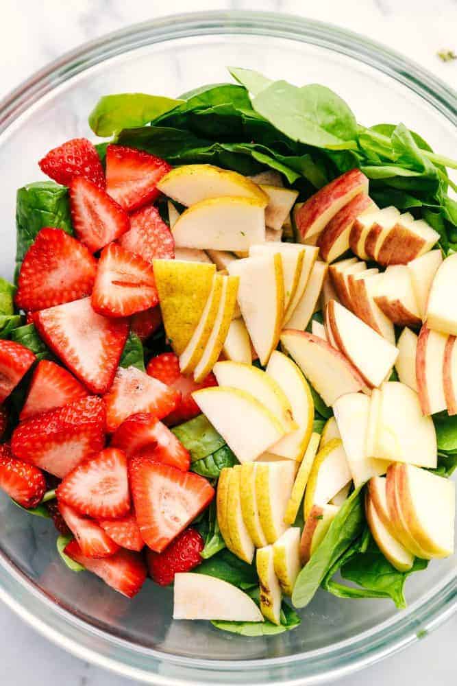 Strawberry, Apple, and Pear Spinach Salad is an easy to make spinach salad with crisp apples, pears and strawberries hidden throughout. Topped with feta cheese, crunchy pecans and tossed in a delicious apple cider dressing! Strawberry, Apple, and Pear Spinach Salad ingredients in a bowl.