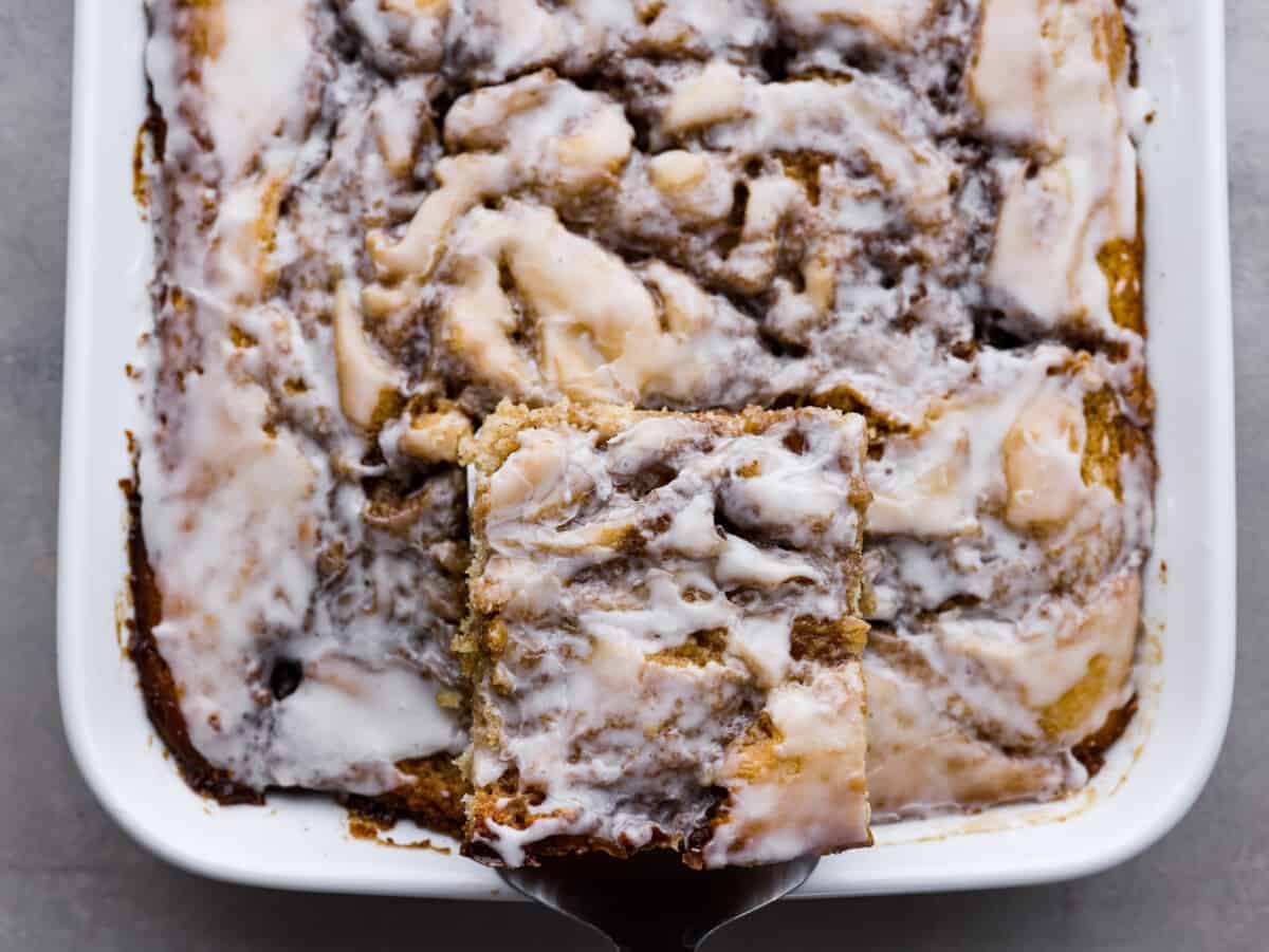 Cinnamon Roll Cakeย is a cinnamon roll turned into an ooey-gooey, delicious cake! Swirled with buttery brown sugar cinnamon and topped with a sweet glazeโฆ this is the BEST cake EVER! Top-down view of a slice of cake being lifted from the pan.