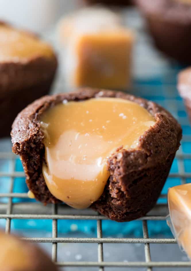 These Salted Caramel Brownie Bites are made with a simple, from-scratch, brownie batter and are filled with a rich (easy to make!) caramel filling! Top everything off with a sprinkle of flaky sea salt for a dessert you'll be coming back to over and over again! Salted Caramel Brownie Bite with caramel pouring out of the top and onto the cooling rack.