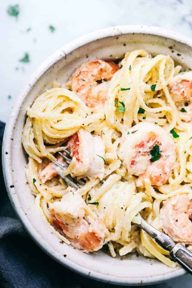 Creamy Garlic Shrimp Alfredo Pastaย is such a classic meal that is brought to its BEST with Shrimp. This meal takes little effort and is so creamy and delicious the entire family will go crazy for!ย Creamy garlic shrimp Alfredo pasta in a white bowl with a fork in the bowl.