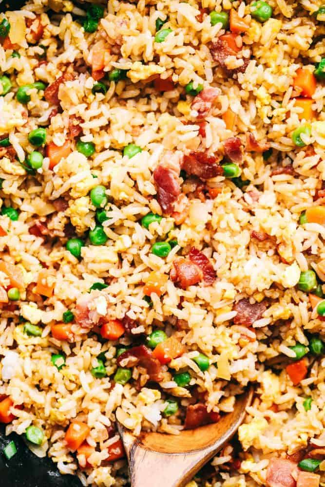 Bacon Fried Rice is 1000x better than takeout and has crispy bacon, eggs, peas, carrots and rice that combine to make the best fried rice ever! Close up of Bacon Fried Rice with a wooden spoon.