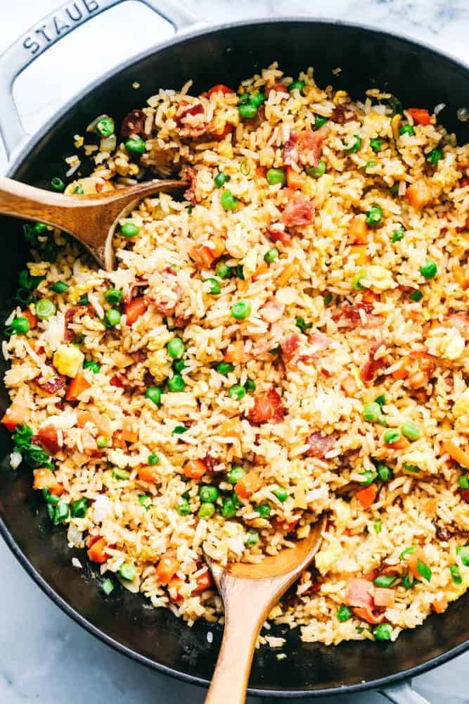 Bacon Fried Rice is 1000x better than takeout and has crispy bacon, eggs, peas, carrots and rice that combine to make the best fried rice ever! Bacon Fried Rice in a skillet with two wooden spoon.