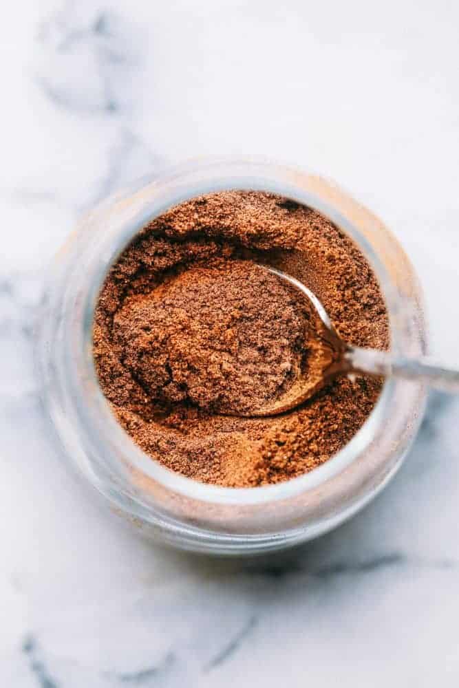 Homemade pumpkin pie spice is a fall spice staple! It's made with cinnamon, ginger, allspice, and nutmeg, which makes it perfect for cakes, pies, and cookies all season long! The top view of pumpkin pie spice in a clear glass jar with a metal spoon.