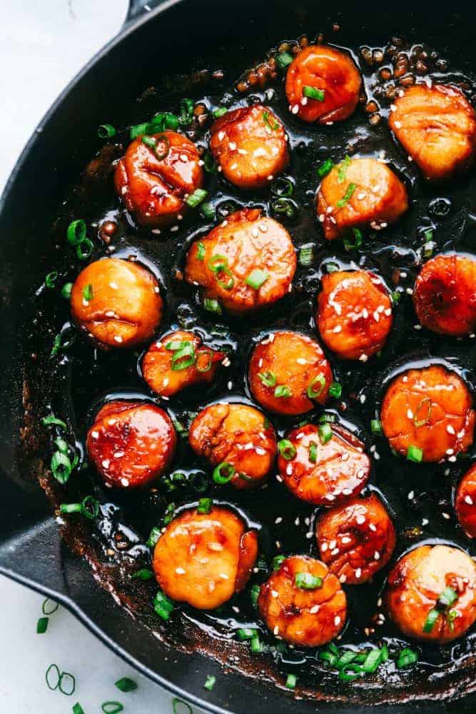 Honey Garlic Butter Scallops get pan seared and then coated in the most amazing honey garlic butter sauce. This meal is so quick and easy that you will make it again and again!ย Honey Garlic Butter Scallops in a skillet.
