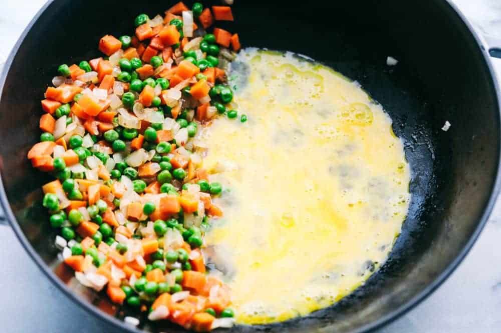 Bacon Fried Rice is 1000x better than takeout and has crispy bacon, eggs, peas, carrots and rice that combine to make the best fried rice ever! Peas and carrot mixture with egg in a frying pan.