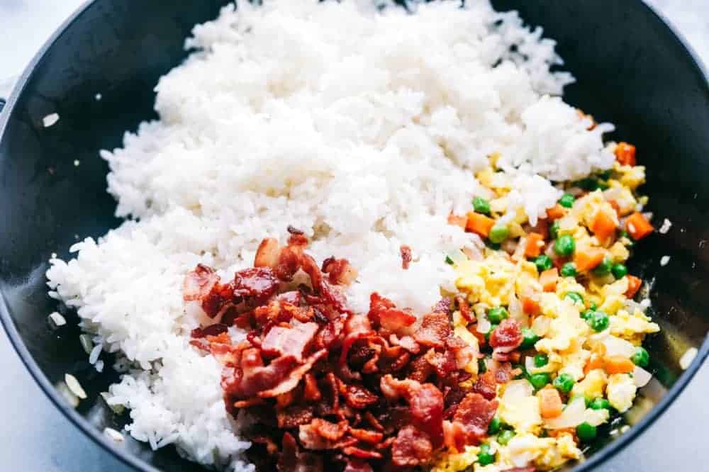 Bacon Fried Rice is 1000x better than takeout and has crispy bacon, eggs, peas, carrots and rice that combine to make the best fried rice ever! Ingredients of Bacon Fried Rice in a pan to be mixed during frying.