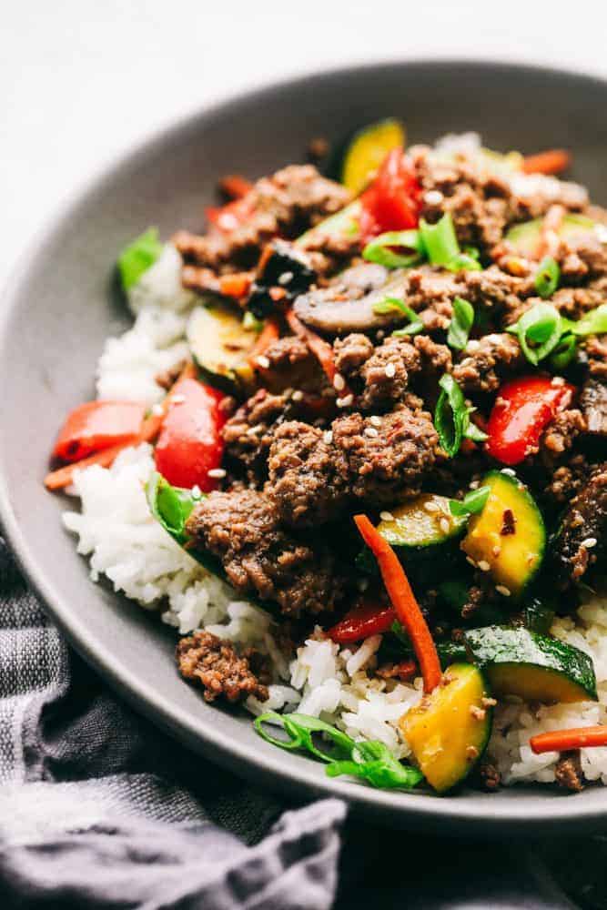 Korean Ground Beef Stir Fry is incredibly easy to make and has the best flavor! This is a recipe that my kids beg me to make every single week!ย Korean ground beef stir fry over top white rice in a gray bowl.