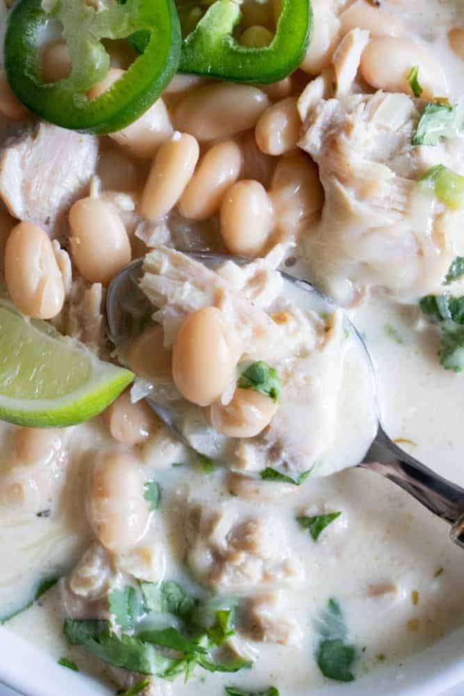 Creamy White Chicken Chili. An easy to make chicken chili recipe that is loaded up with juicy, tender bites of chicken, white beans, green chiles and jalapeno. All in a flavorful, creamy broth. Bowl full of Creamy White Chicken Chili with a spoon.