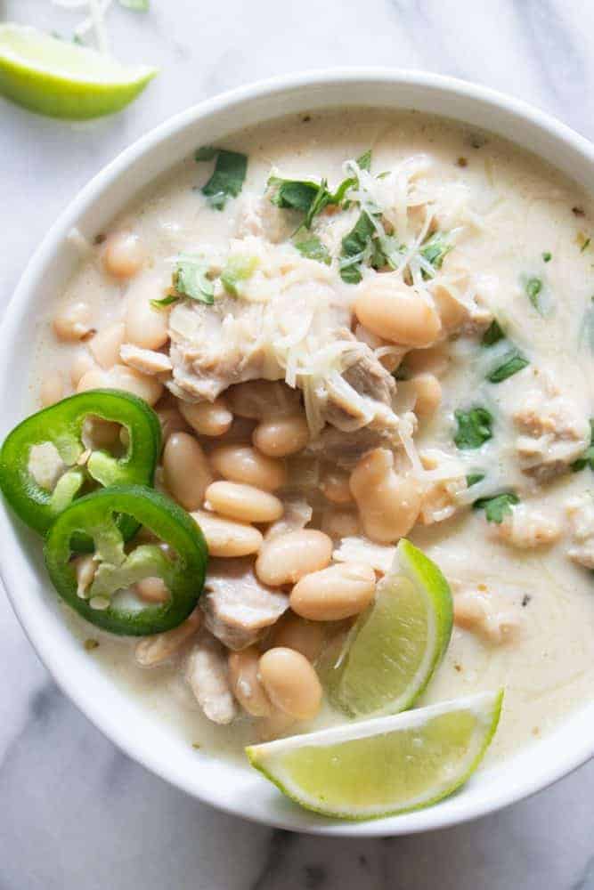 Creamy White Chicken Chili. An easy to make chicken chili recipe that is loaded up with juicy, tender bites of chicken, white beans, green chiles and jalapeno. All in a flavorful, creamy broth. White bowl of Creamy White Chicken Chili with freshly sliced jalapeño and lime on top.