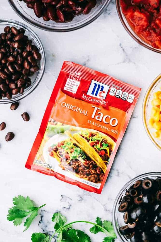 Cheesy Taco Soup is so simple to throw together and is loaded with taco inspired ingredients. The cheesiness takes this soup to the next level of delicious and will be loved by the entire family! Ingredients of Cheesy Taco Soup with a packet of McCormick Taco Seasoning Mix in the middle.