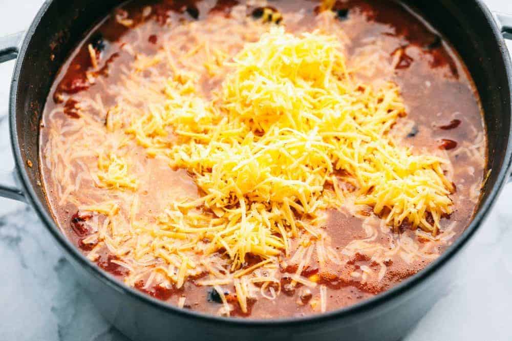 Cheesy Taco Soup is so simple to throw together and is loaded with taco inspired ingredients. The cheesiness takes this soup to the next level of delicious and will be loved by the entire family! Large pot of Cheesy Taco Soup with freshly grated cheese on top.